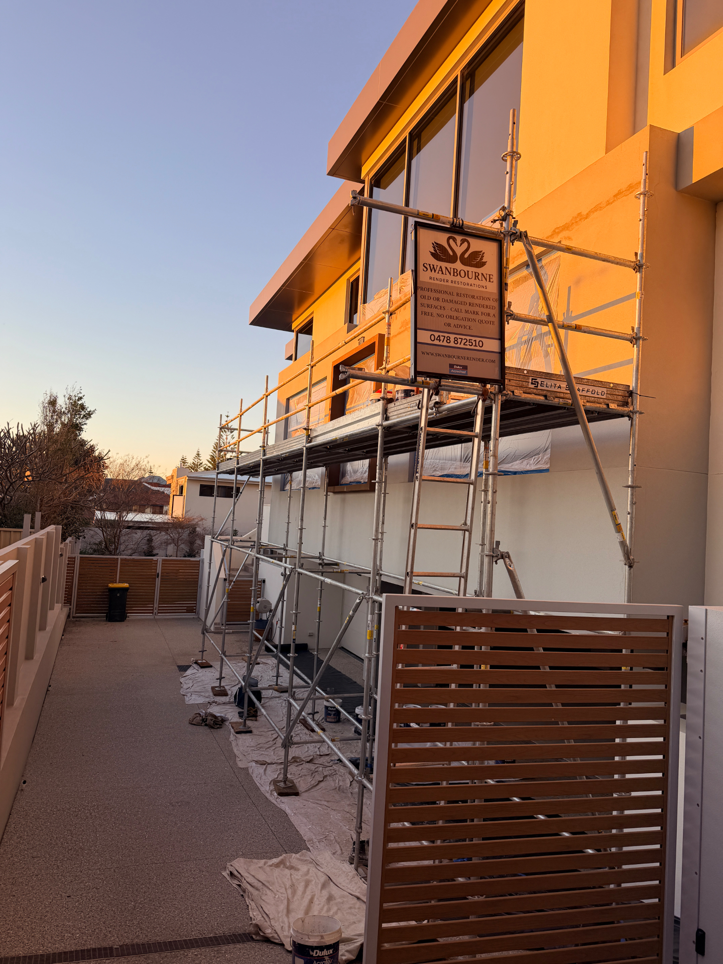 Scaffolded North Beach facade during render repair works at sunset