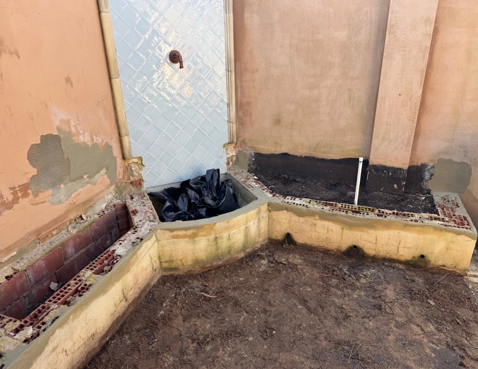 Bicton courtyard corner before works, showing patched render and deteriorated garden bed walls